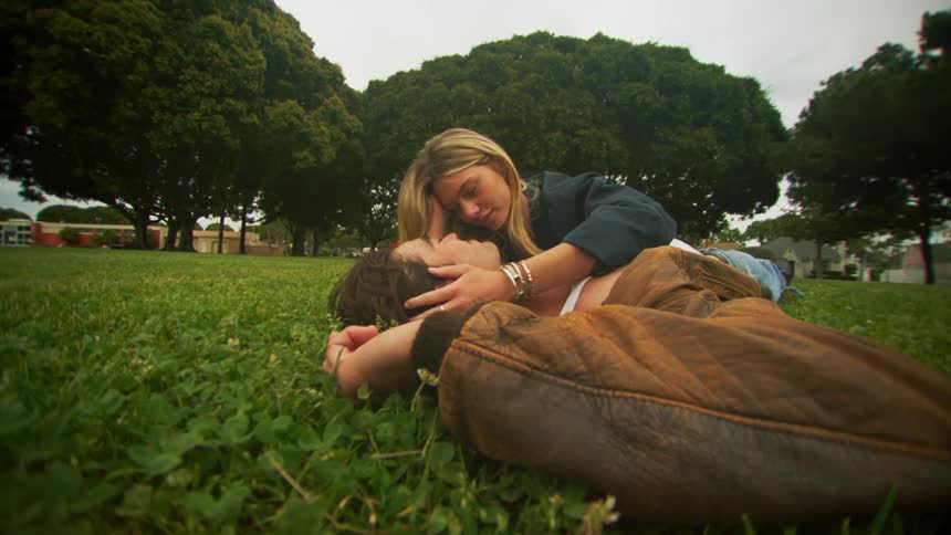 Couple lying on the grass kissing romantically against a cloudy sky