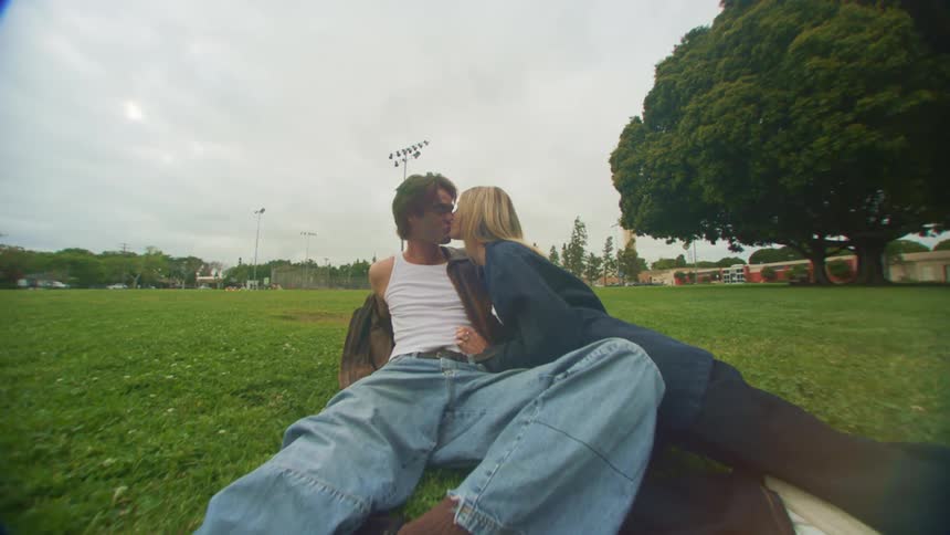 Man and woman sitting on the grass in a park kissing