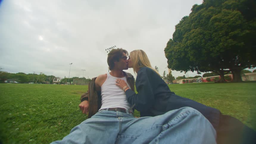 Man and woman lying on the grass in the park smile and kiss
