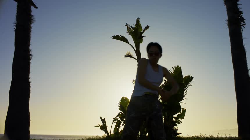 Man dancing in a natural environment against a late afternoon sun and with trees around