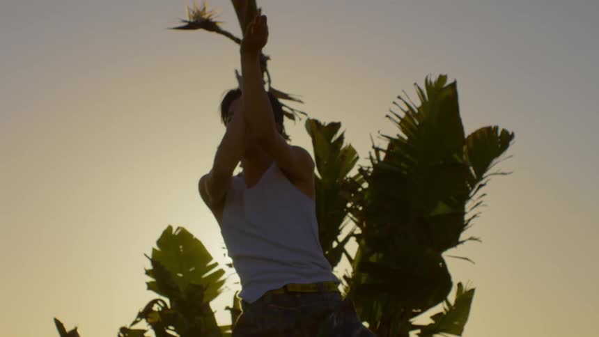 Man dancing moving his arms in front of a tropical tree with sunlight