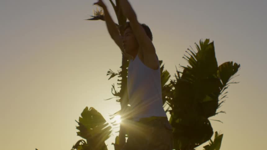 Young man in a tank top dancing artistically against a late afternoon sky with reflected sunlight