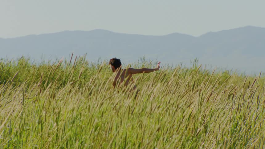 Man and a hill with the bush dancing shirtless and the silhouette of the mountains on the horizon