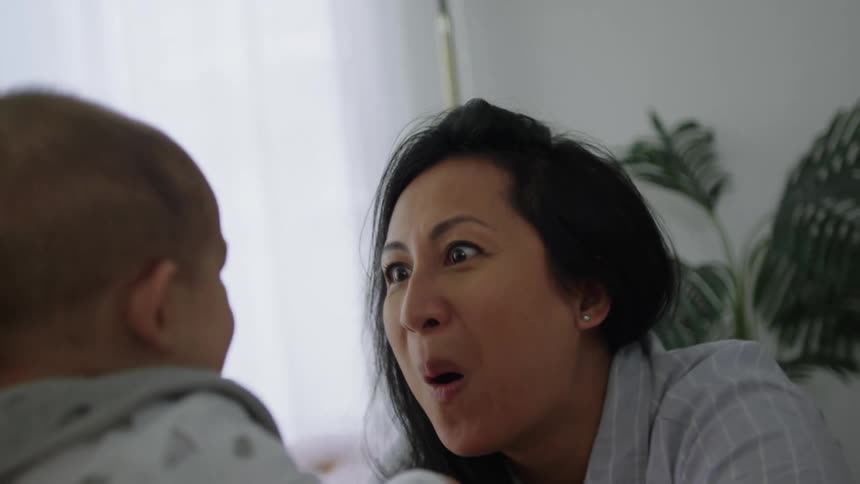 Smiling mother playfully makes faces and moves her child while at home