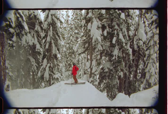 Skier wearing a red jacket and pants stands on a snow hump in the snowy forest