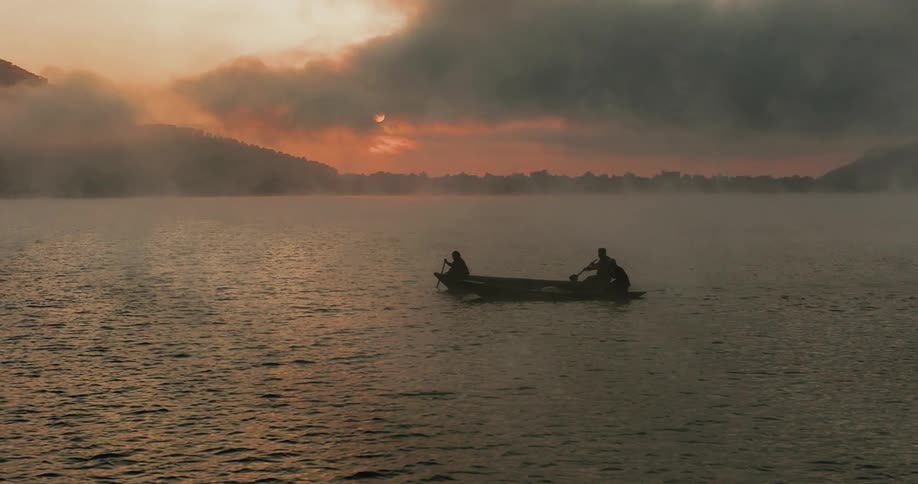 People in a canoe in the middle of the calm sea against a cloudy reddish sky