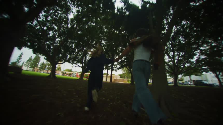 Man and woman holding hands running in a park with trees