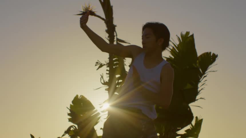 Dancer man moving his arm in artistic movement next to tropical vegetation with a reflection of sunlight
