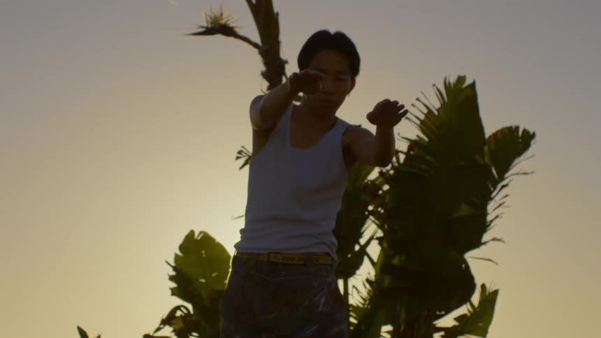 Young man dancing in front of a tree and with sunlight reflection