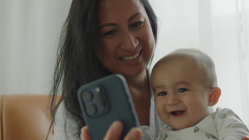 Portrait of mother holding her baby on her lap and taking a selfie