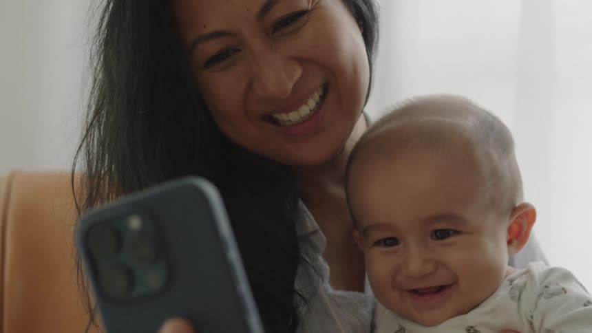 A mother and her child smile and laugh while looking at a smartphone screen