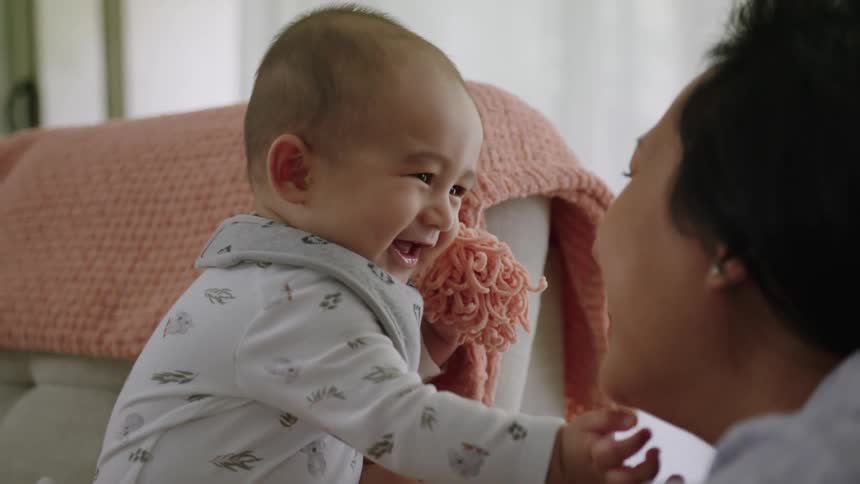 A woman holding a baby playing with them as both laugh