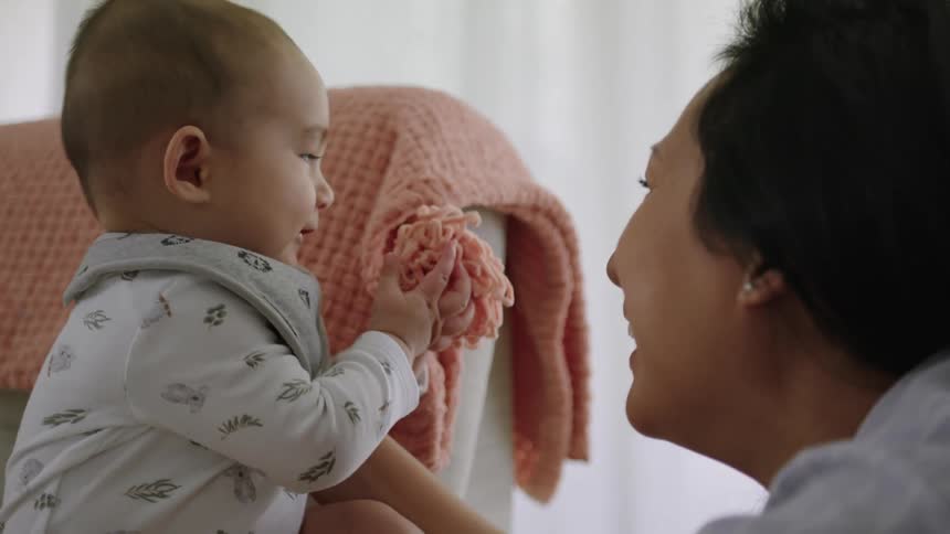 Mother playing with her baby who is sitting on the couch holding a blanket