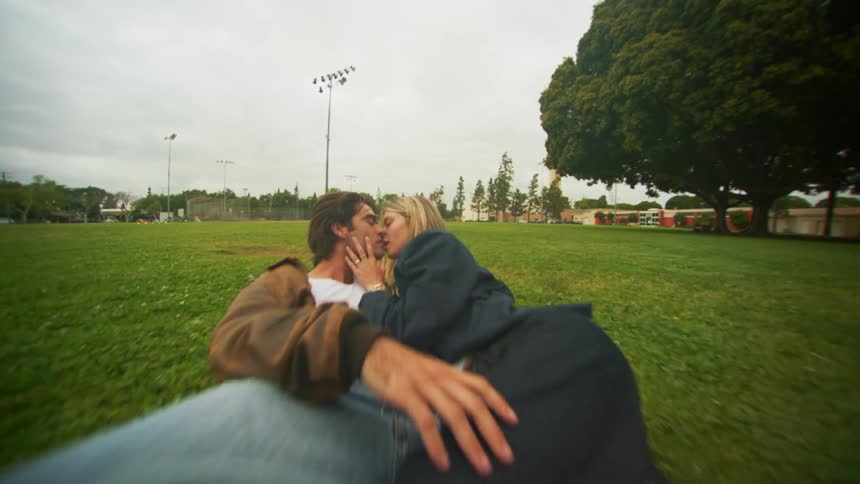 A couple kissing while lying in the grass in a park