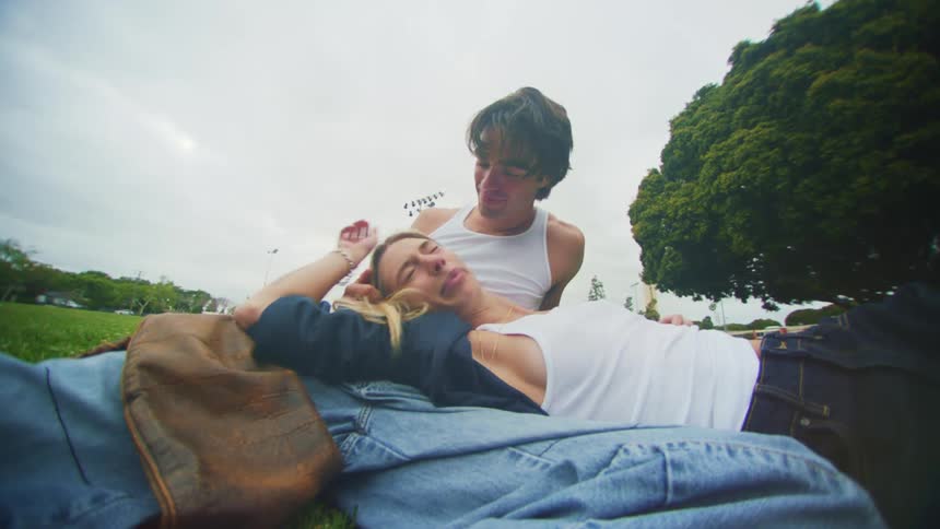 Man and woman smile at each other while on the ground in park then she sits up