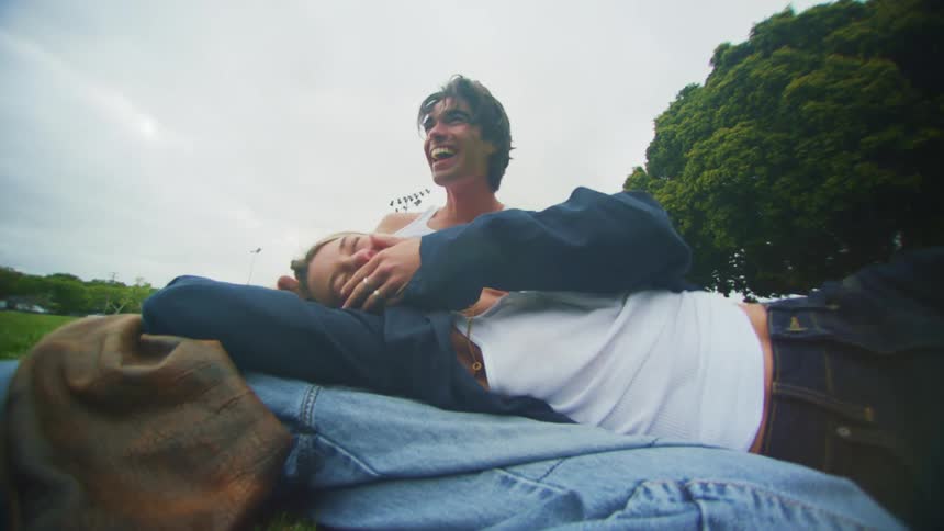 Woman lying on the lap of a man who is sitting on the grass in a park while smiling and having fun
