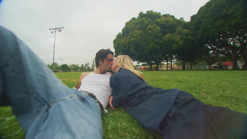 Man and woman lie on the grass in the park kissing
