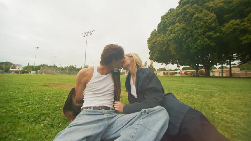 A young couple kissing over the green grass in the park