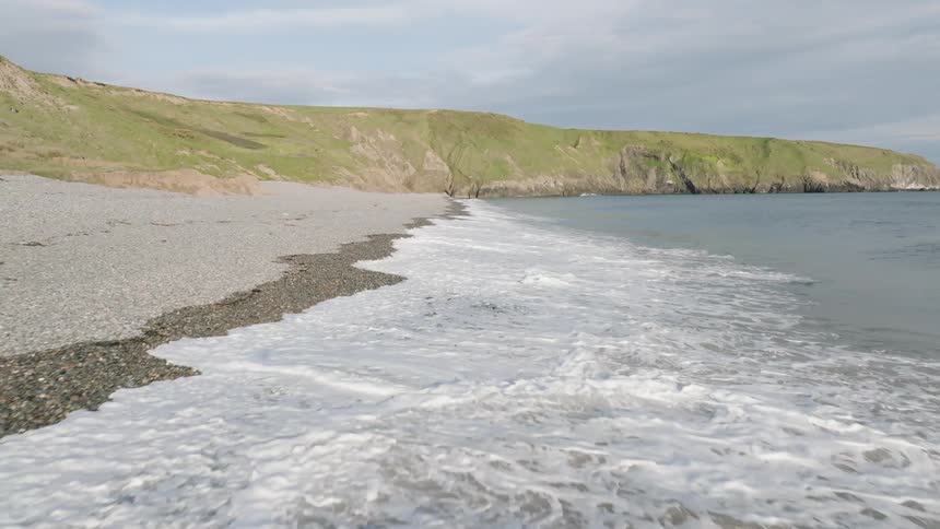Landscape of a beach with waves and the greenish coast