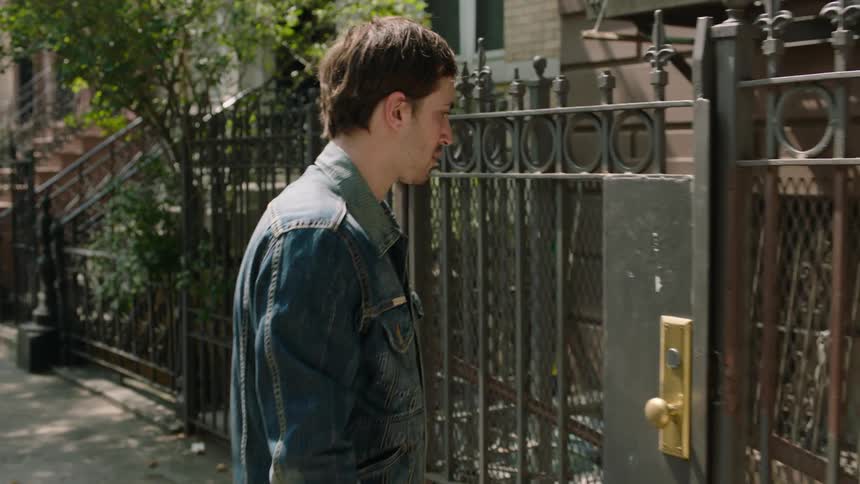 A man is walking down a city street and checking an iron gate