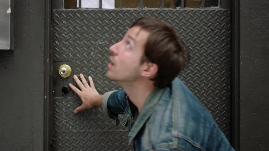 A man walks up to a steel door and dodges falling objects