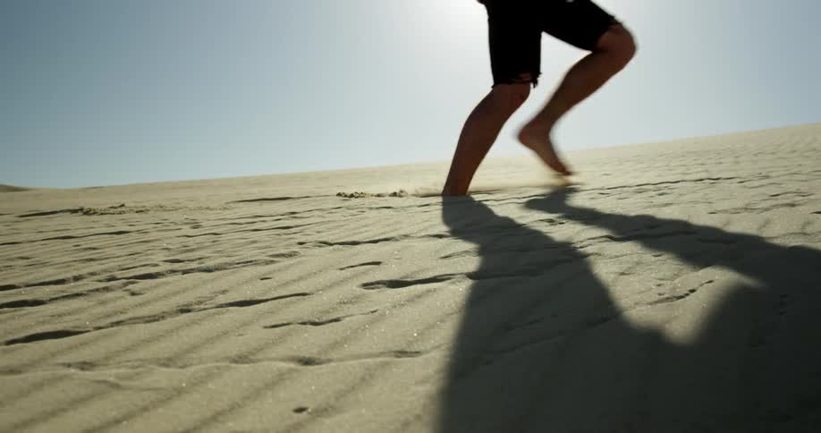 A man walks barefoot through desert sand as the sun beats down