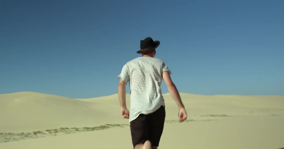 A man runs in the desert and loses his hat