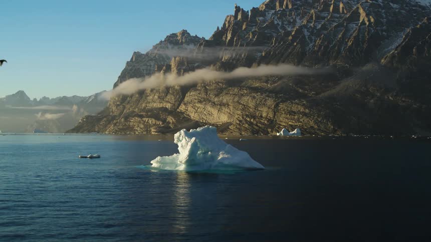 Aerial view of an iceberg floating on the water next to a mountainous coastline