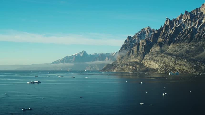 Landscape of a wet black land with sharp mountains around and with pieces of ice around
