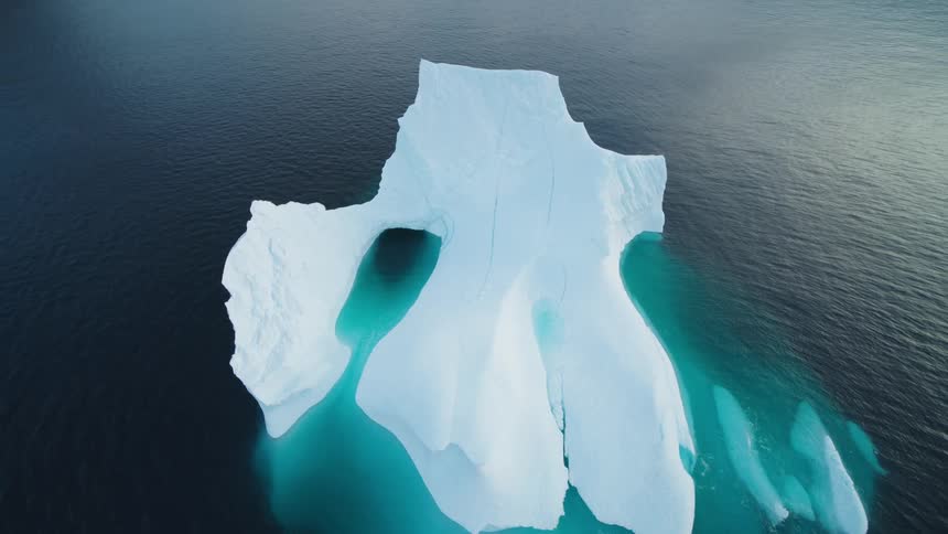 Aerial view of a large iceberg floating in the ocean with a larger submerged section in clear waters