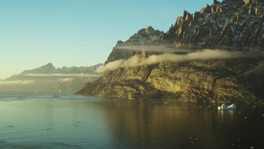 Landscape of rocky mountains with sharp peaks under golden sunlight and with small icebergs