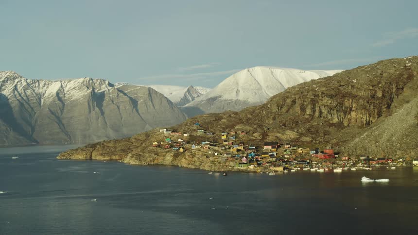 Aerial panorama of waters on a terrain of black earth and the edge of mountains with snow and a village
