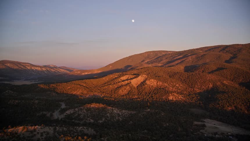 Aerial panorama of a mountain valley with vegetation in a purple sky and with the moon visible