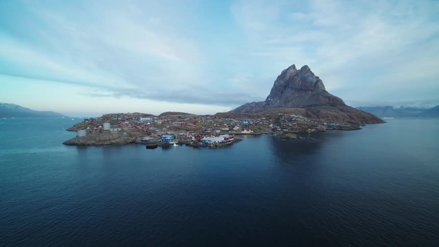 Aerial panorama of an iceberg in the middle of the sea and in the background a village on an island