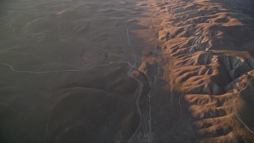 Aerial view of a rugged landscape with undulating hills and valleys during golden hour sunlight