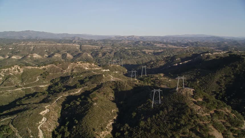 Aerial panorama of electricity transmission towers amid wooded hills and mountains