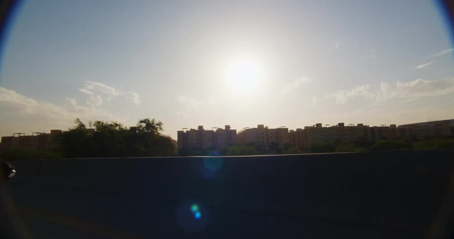 A view from a moving vehicle showing an urban landscape with buildings under a bright sun