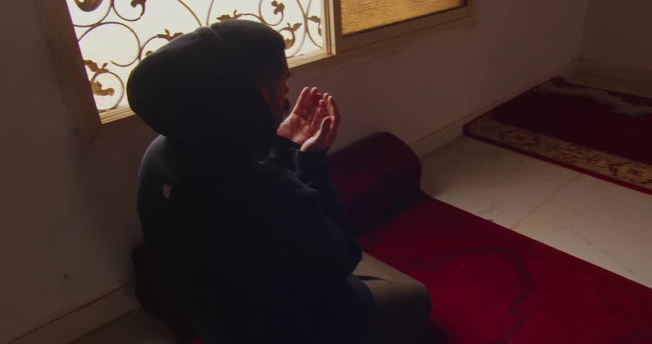 Man kneeling on the ground with his hands leaning against each other praying in a temple