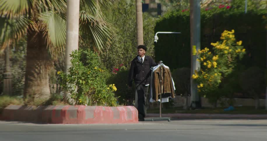 A man pushes a rack full of clothing down the street