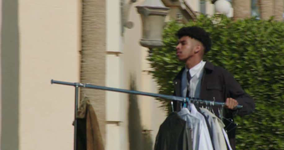 Young black man walking across a busy street pushing a clothes rack