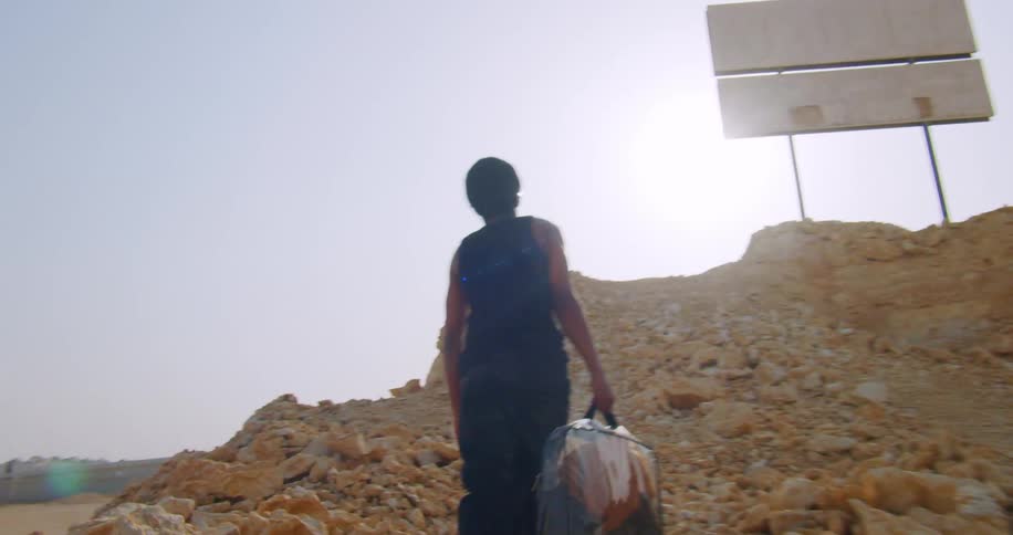 Back view of a man climbing rocks on a hill with a signpost above
