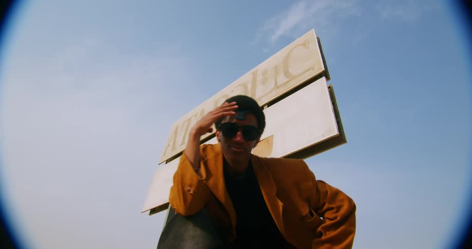 A young male kneels and poses modeling clothing and jewelry