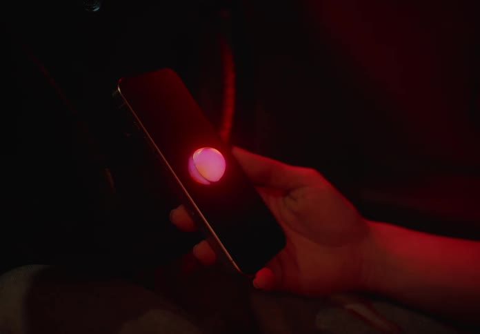 Closeup of a persons hand holding a smartphone and a small abstract luminous ball coming out of the screen