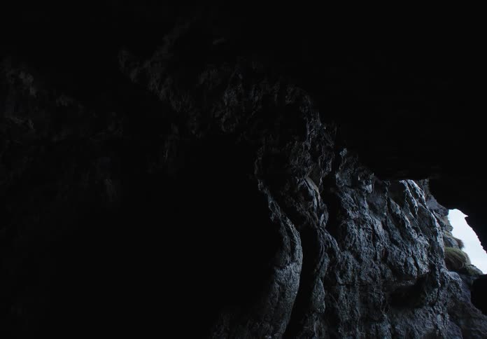 The interior of a stone cave with an opening showing the outside which is a coast