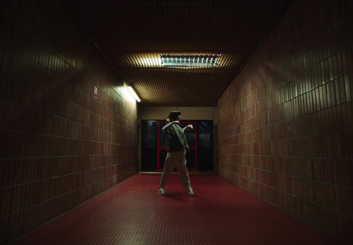 A young person dances in a dimly lit corridor with tiled walls