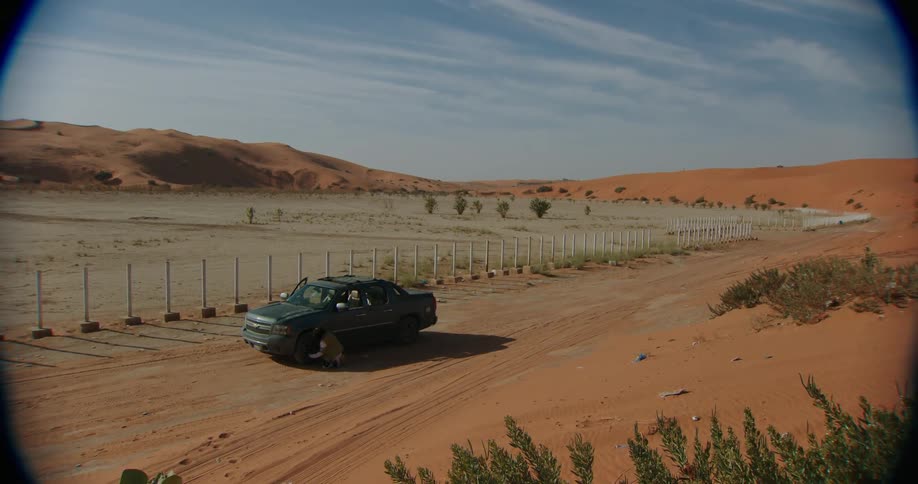 Man checks the black pickups tire near the fences in the desert