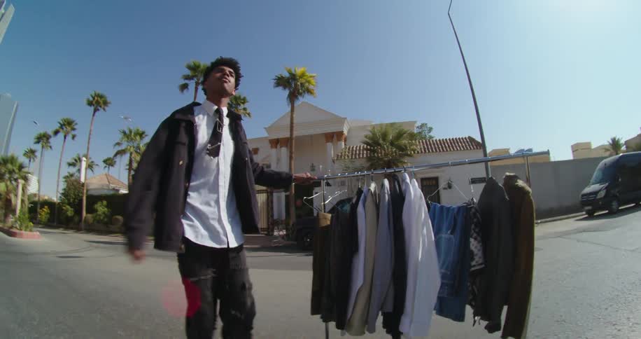 A black man rolls a rack of clothes down a street