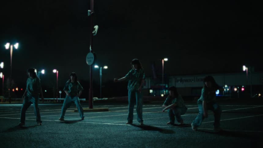 Clones of the same woman dancing in a parking lot at night