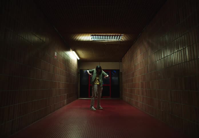 An asian girl performs an odd dance in a hallway