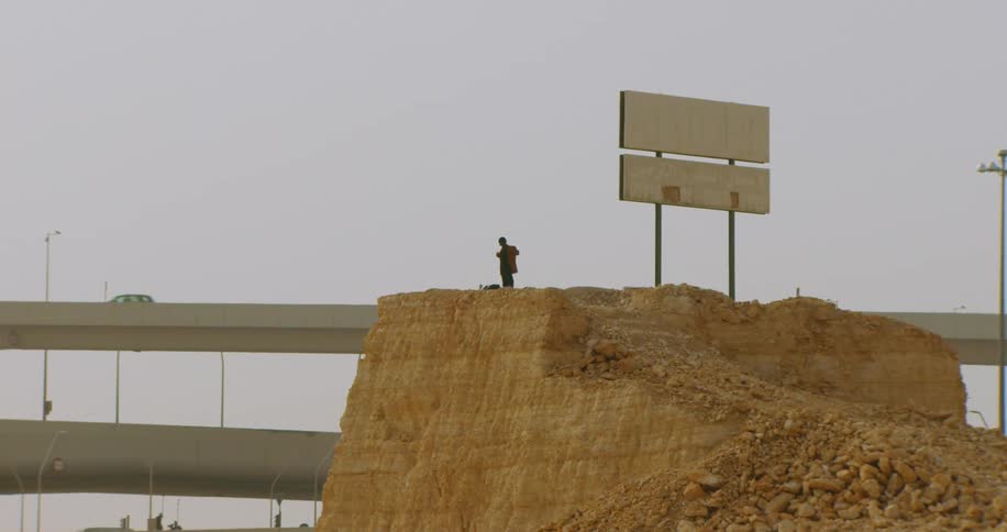 A man dresses himself while standing on a large mound near overpasses